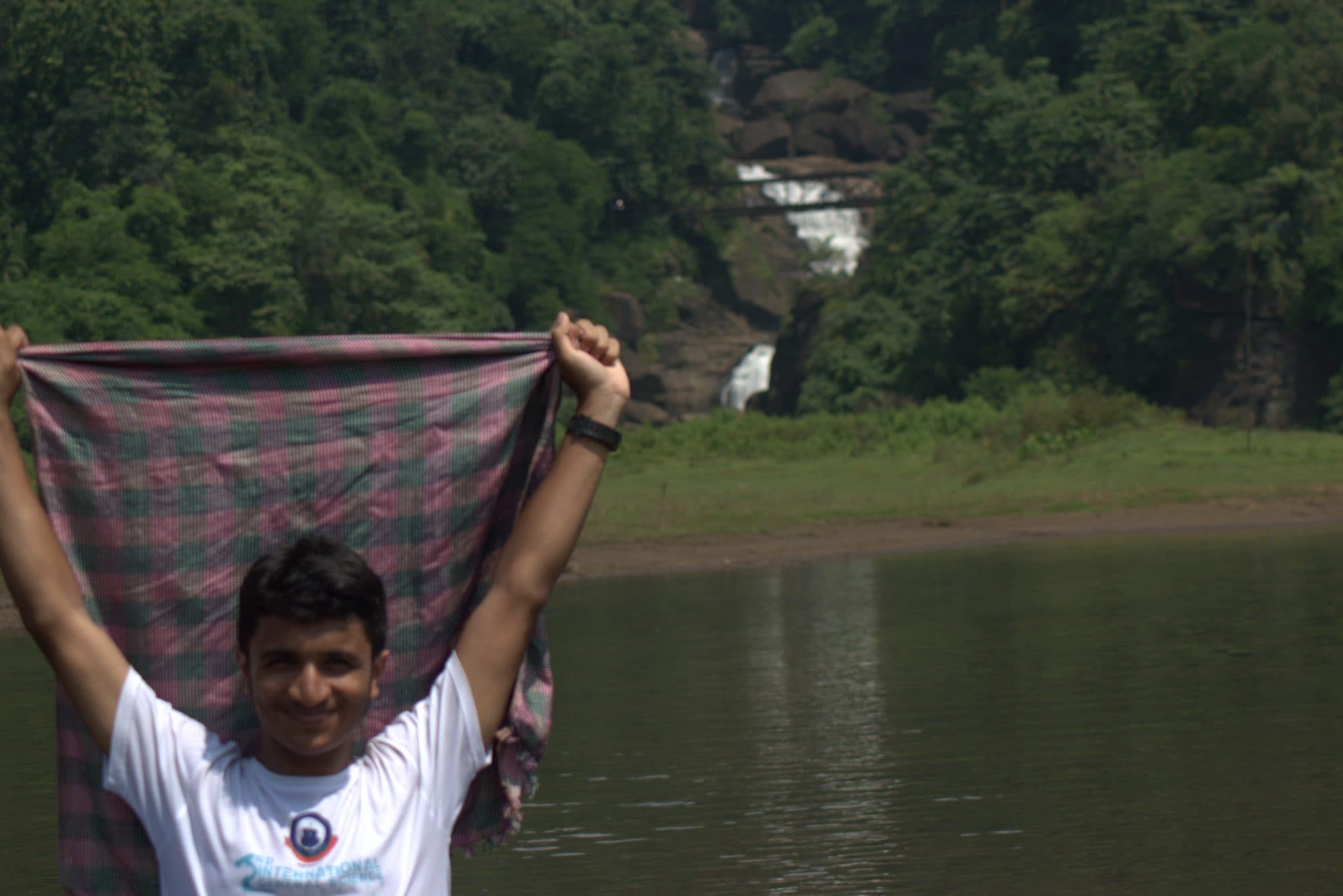Mohammad Nasir raising a gamchha by a lake below a waterfall in Sylhet